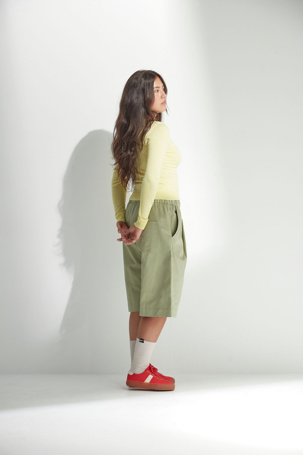 Woman wearing a light yellow cardigan and wide-leg shorts on a white background