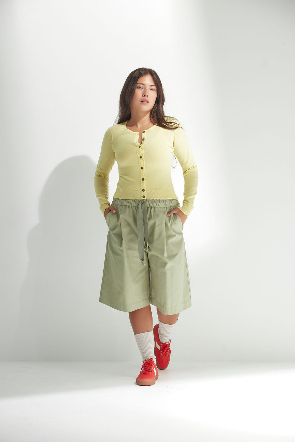 Woman wearing a light yellow cardigan and wide-leg shorts on a white background