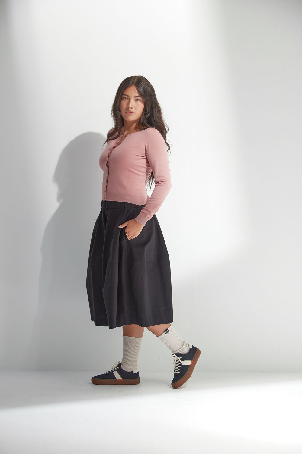 Woman wearing a pink sweater and black skirt on a white background