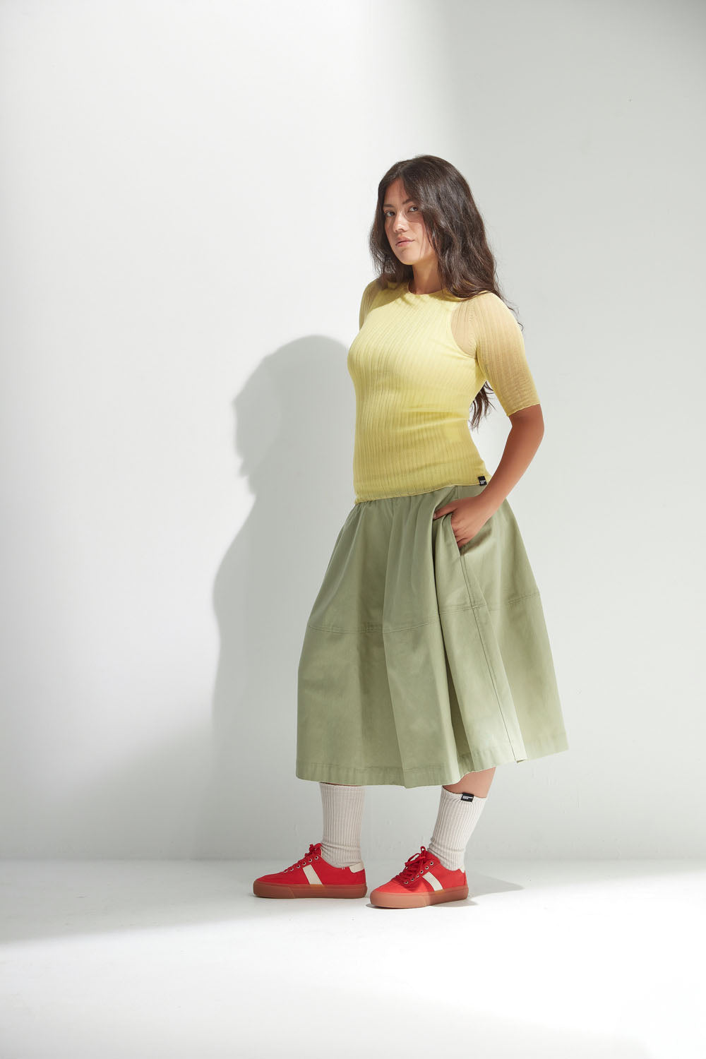 Woman wearing a yellow tulle top and green skirt with red shoes on a white background