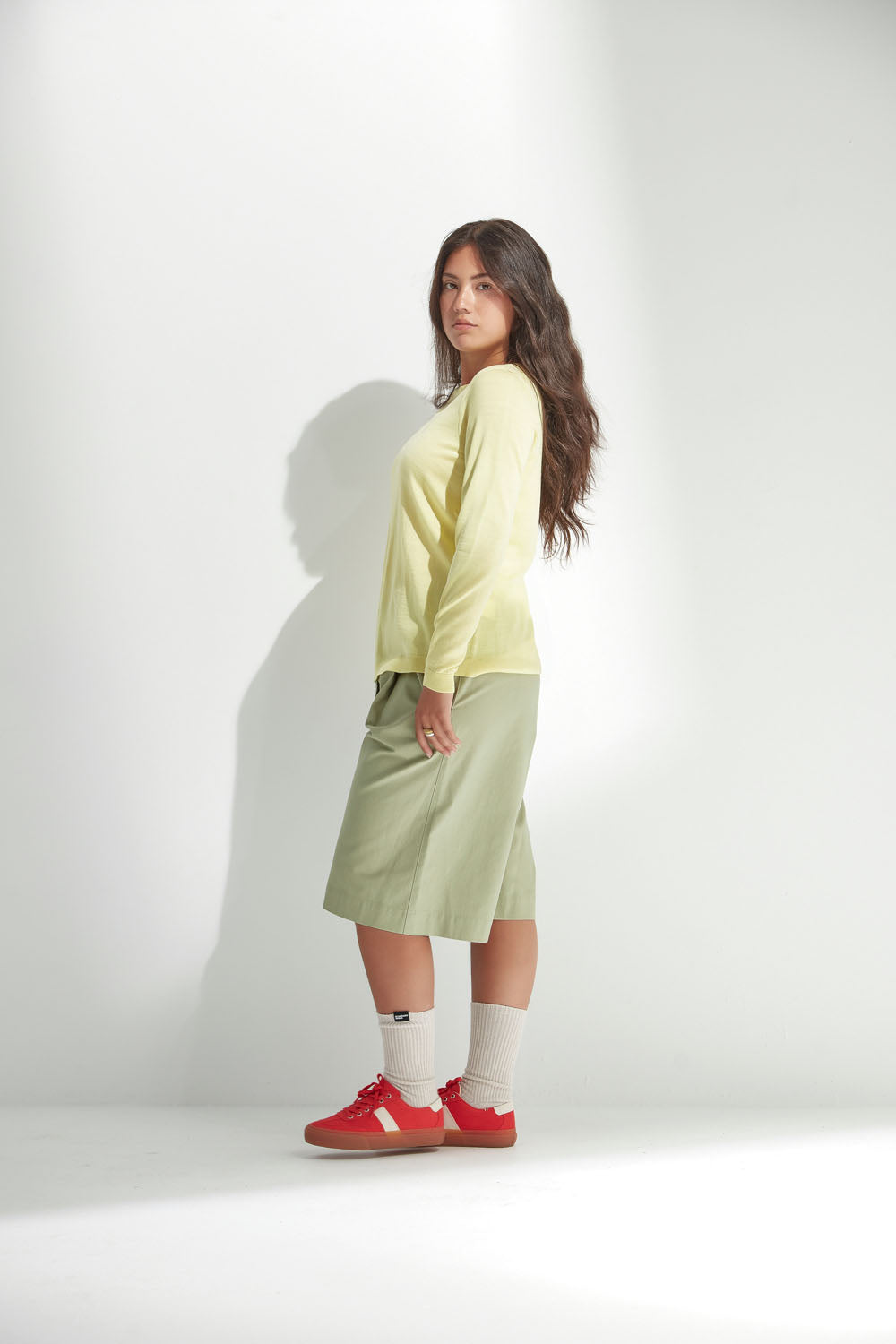 Woman wearing a light green sweater and shirts with red shoes on a white background
