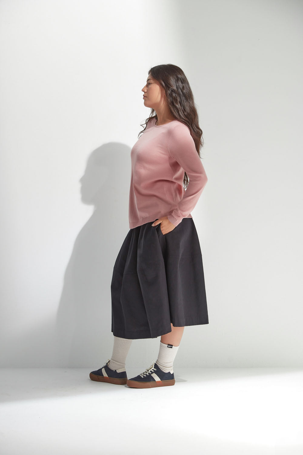 Woman wearing a pink sweater and black skirt against a white background