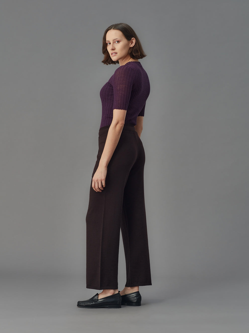 Woman wearing a purple tulle top and dark pants against a gray background