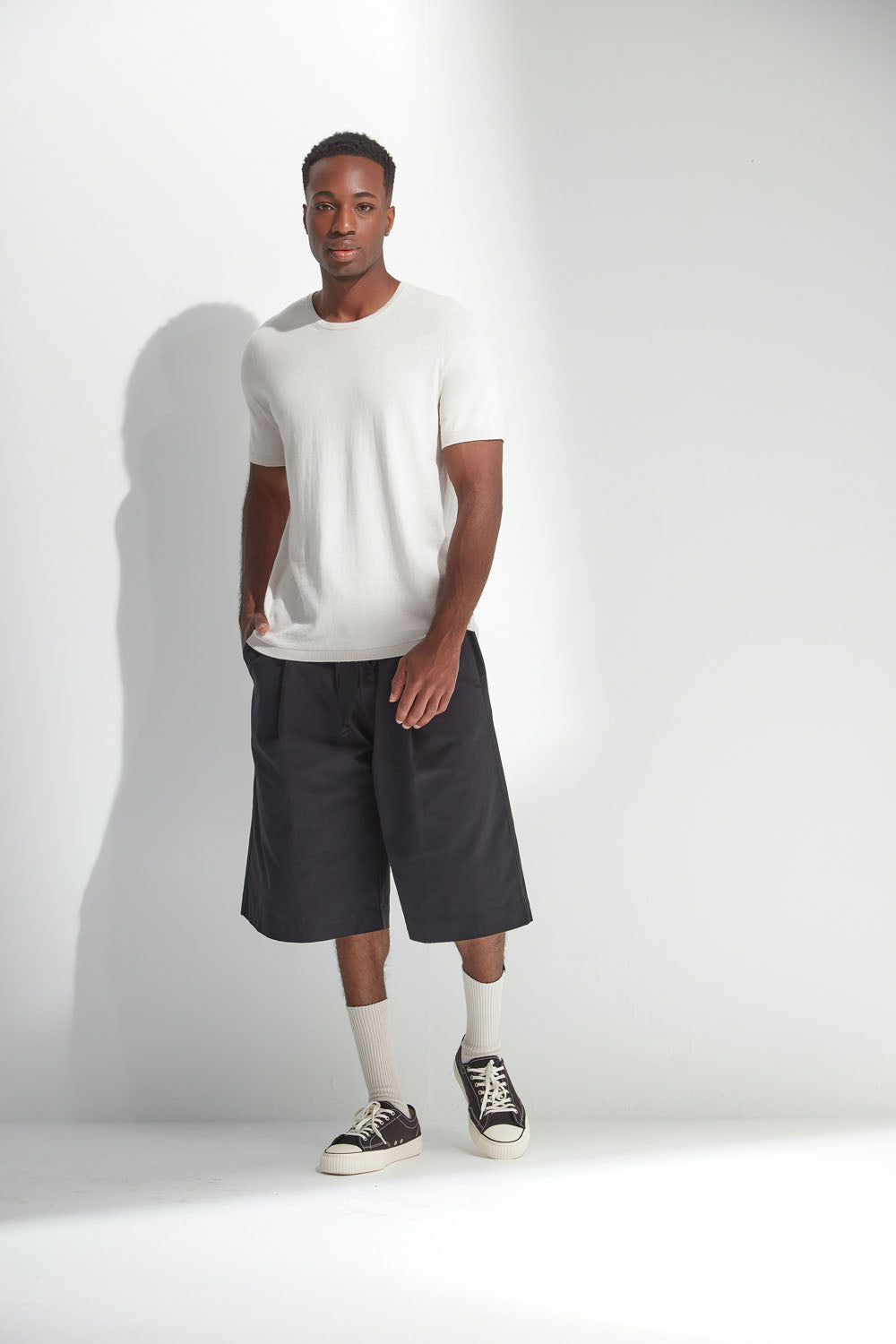 Man wearing a white t-shirt, dark shorts, and black sneakers on a white background