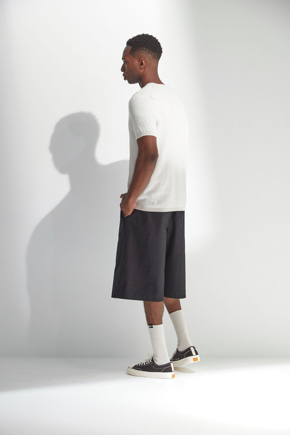 Man wearing a white t-shirt, dark shorts, and black sneakers on a white background