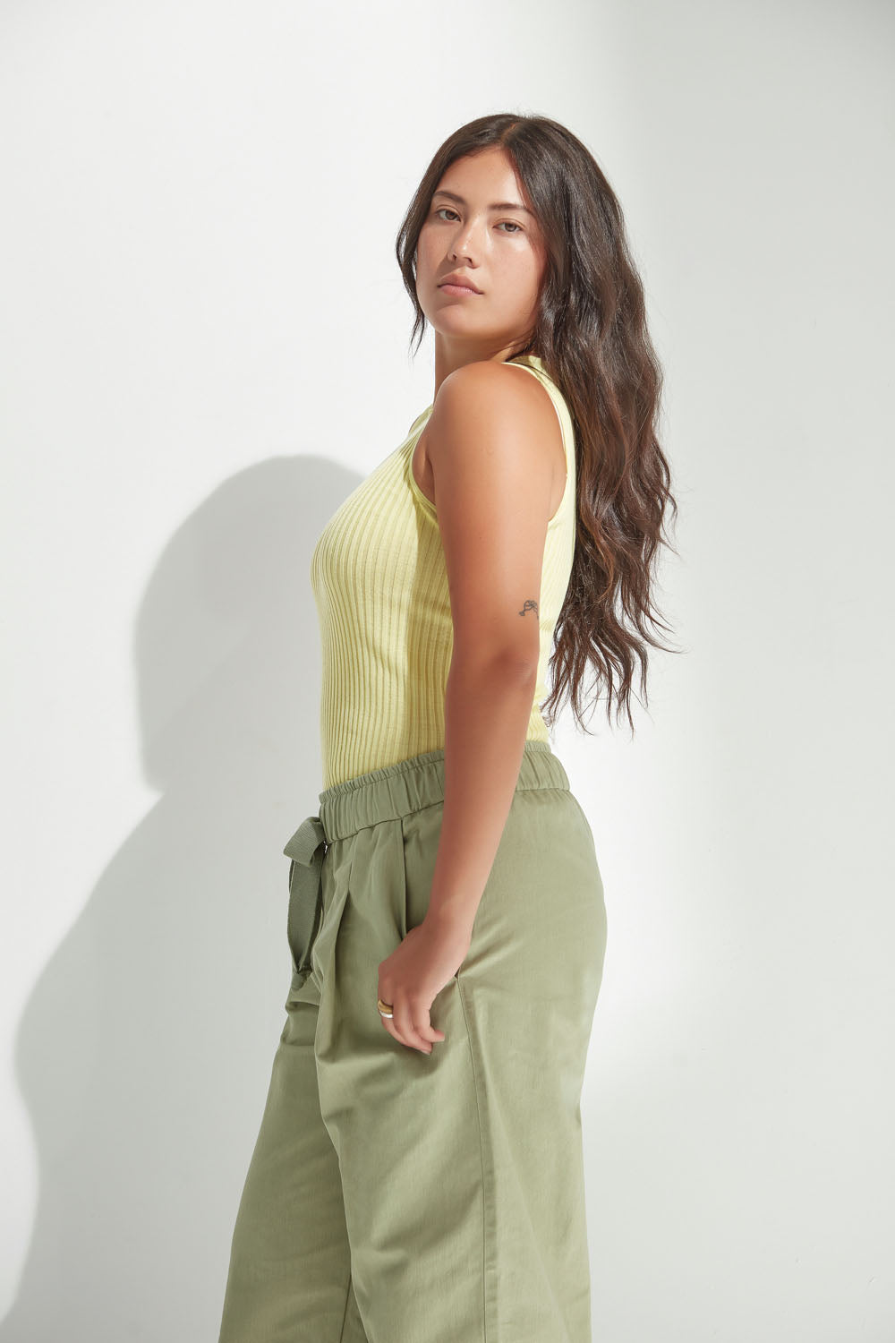 Woman wearing a yellow sleeveless top and green pants against a white background