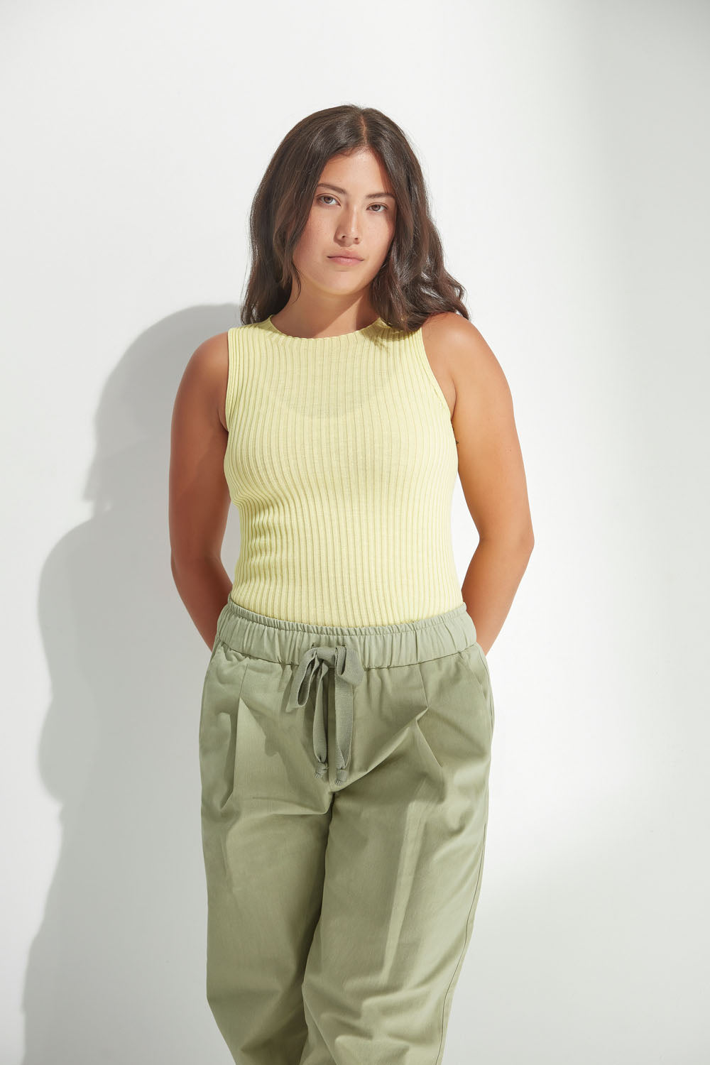 Woman wearing a yellow sleeveless top and olive green pants against a white background