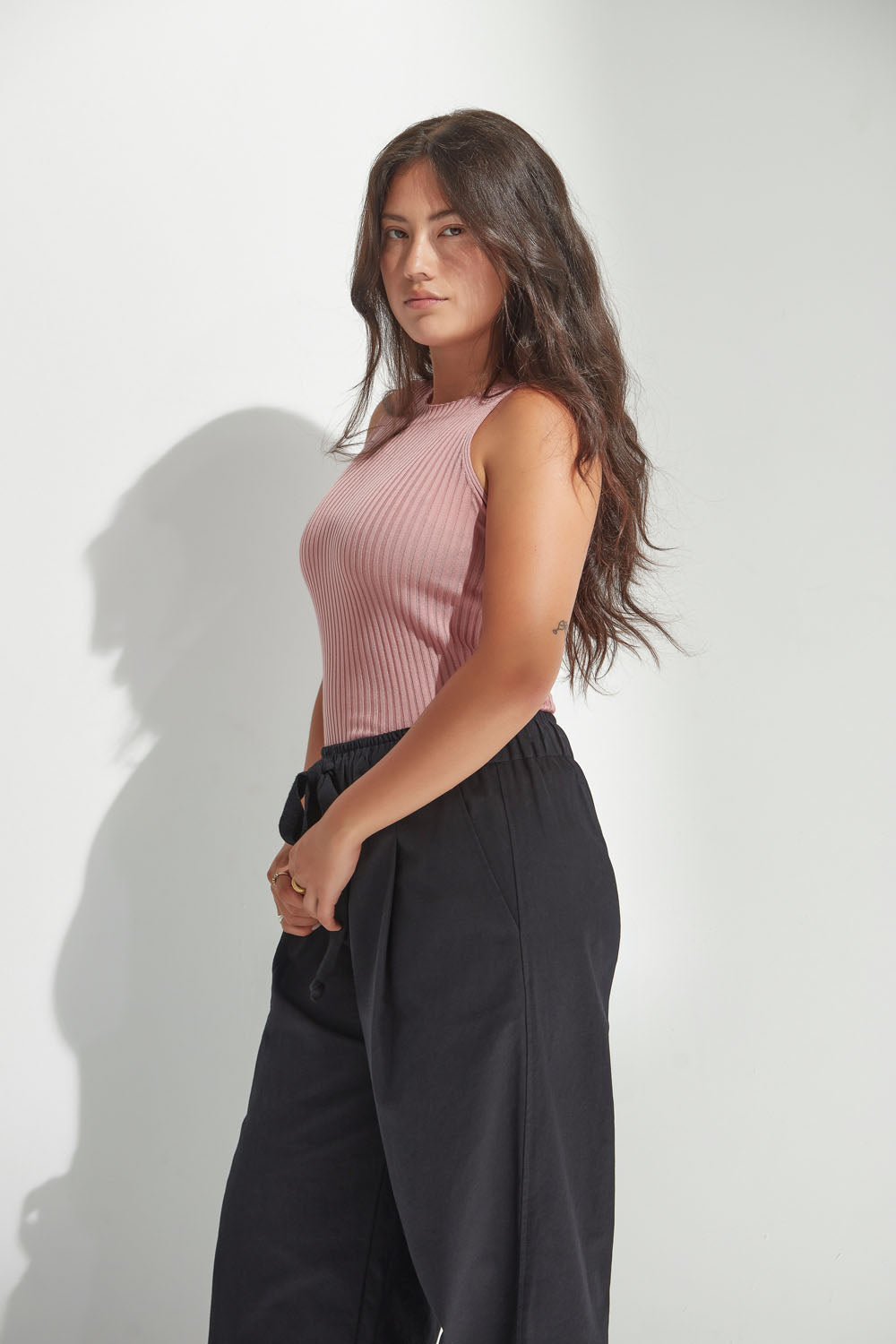 Woman wearing a pink sleeveless top and black pants against a white background