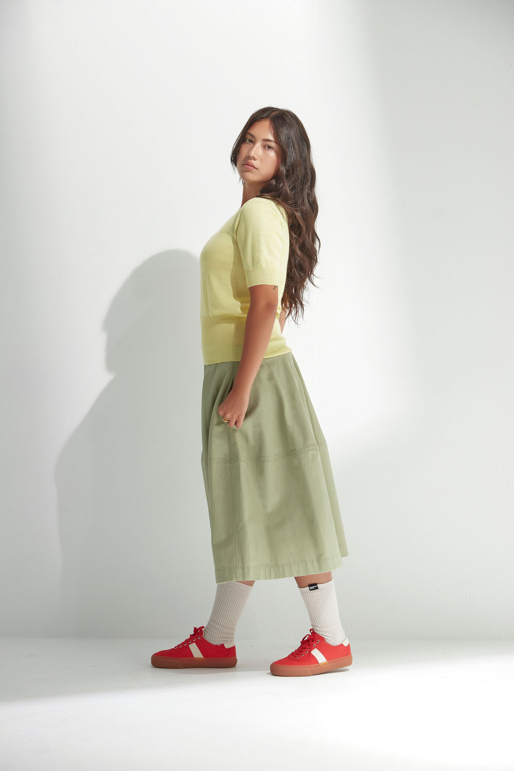 Woman wearing a yellow top and green skirt with red shoes on a white background
