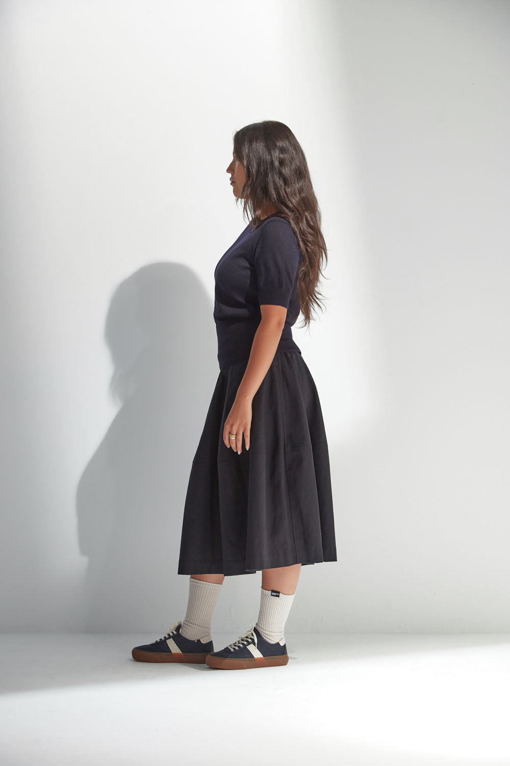 Woman wearing a navy top and skirt standing against a white wall