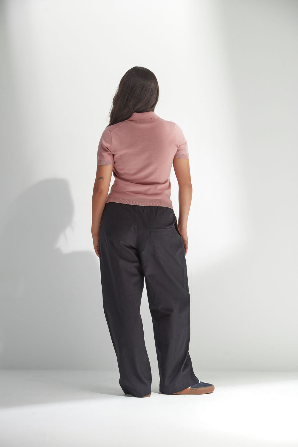Woman wearing a pink top and dark pants against a white background