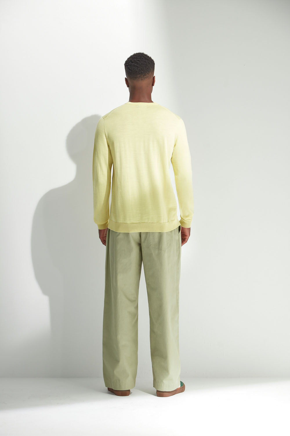 Man wearing a light yellow sweater and green pants against a white background