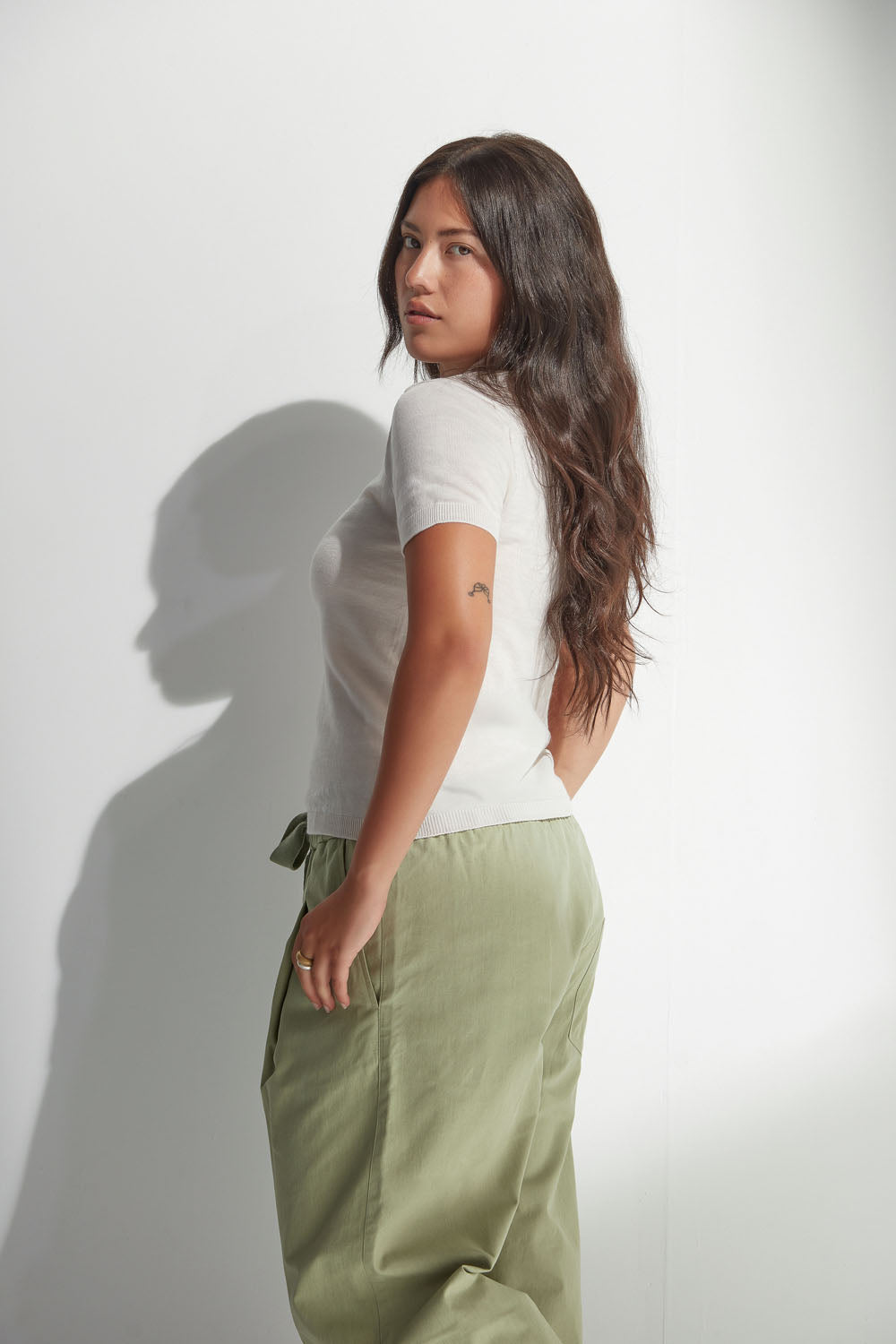 Woman wearing a white polo and green pants against a plain background