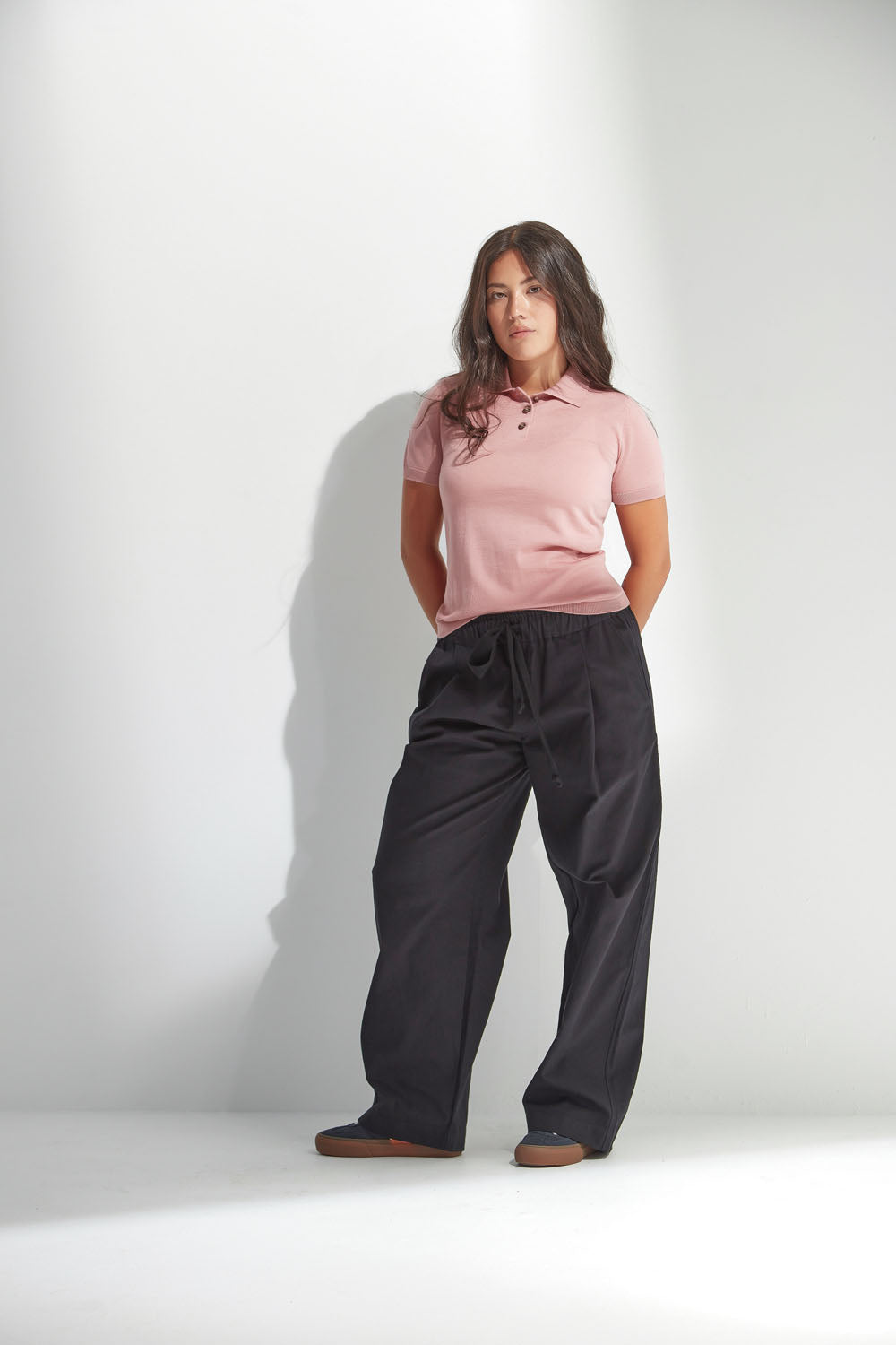 Woman wearing a pink polo shirt and black pants against a white background