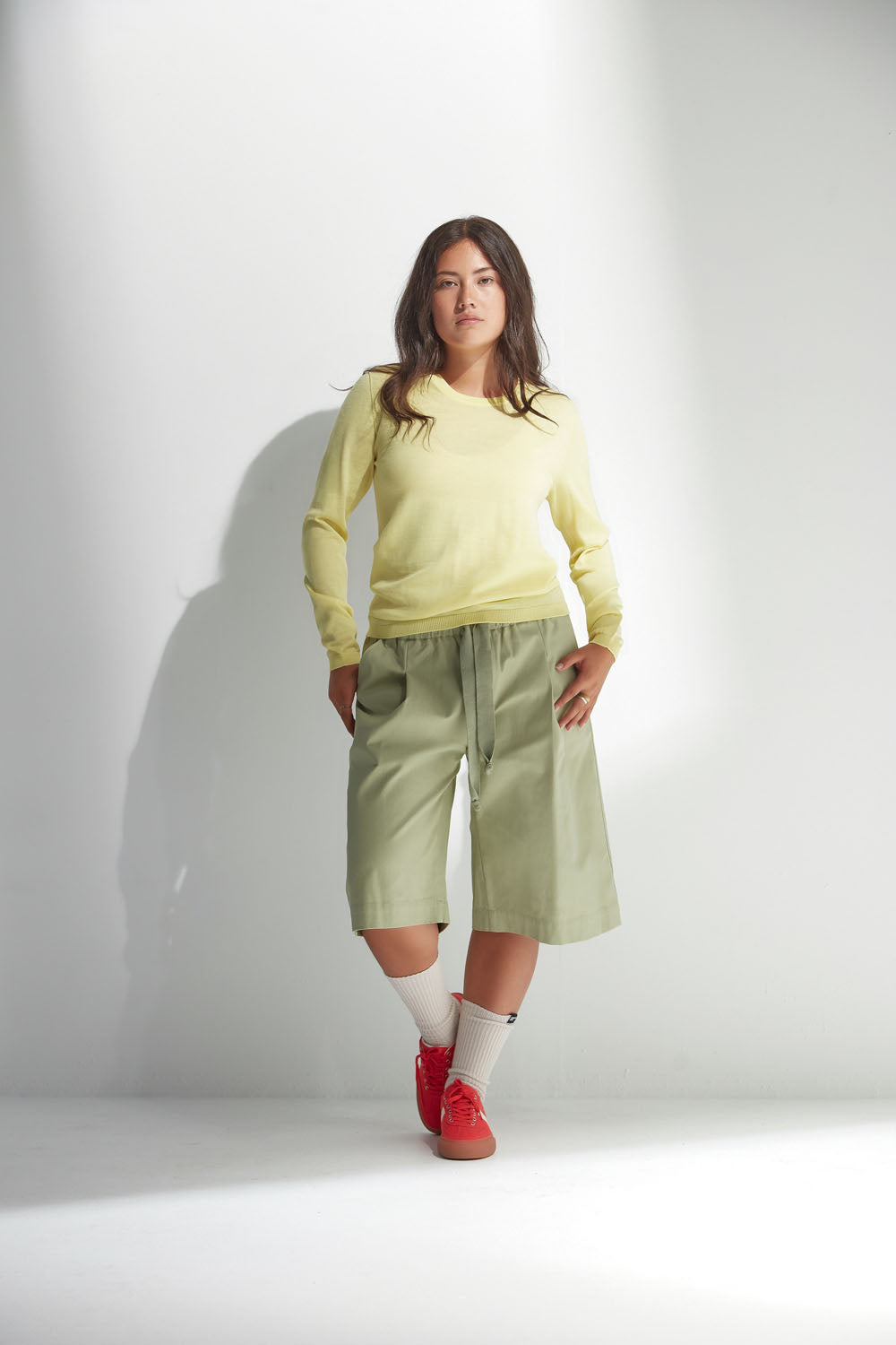 Woman wearing a light yellow sweater and green shorts against a white background