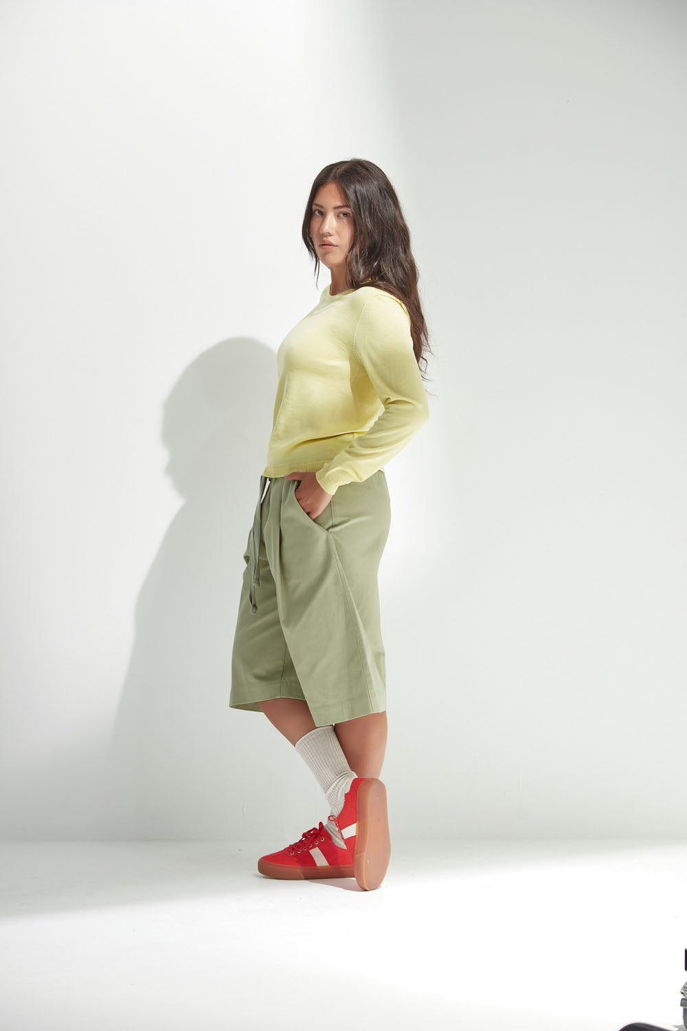 Woman wearing a light yellow sweater and green shorts against a white background