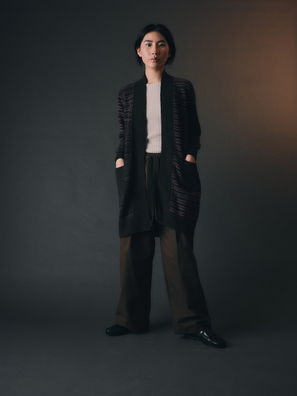 Woman wearing a long, dark stripe-patterned cardigan against a dark background
