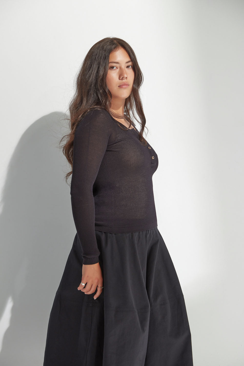 Woman wearing a black long-sleeve top and black skirt against a white background