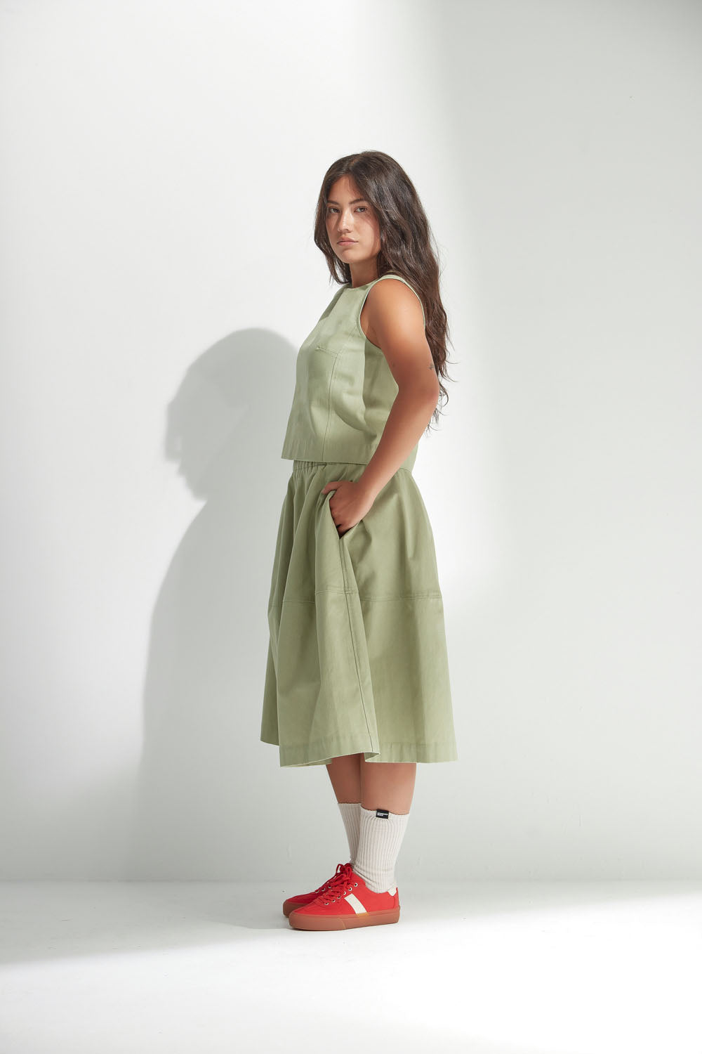 Woman wearing a light green top and skirt with red shoes on a white background