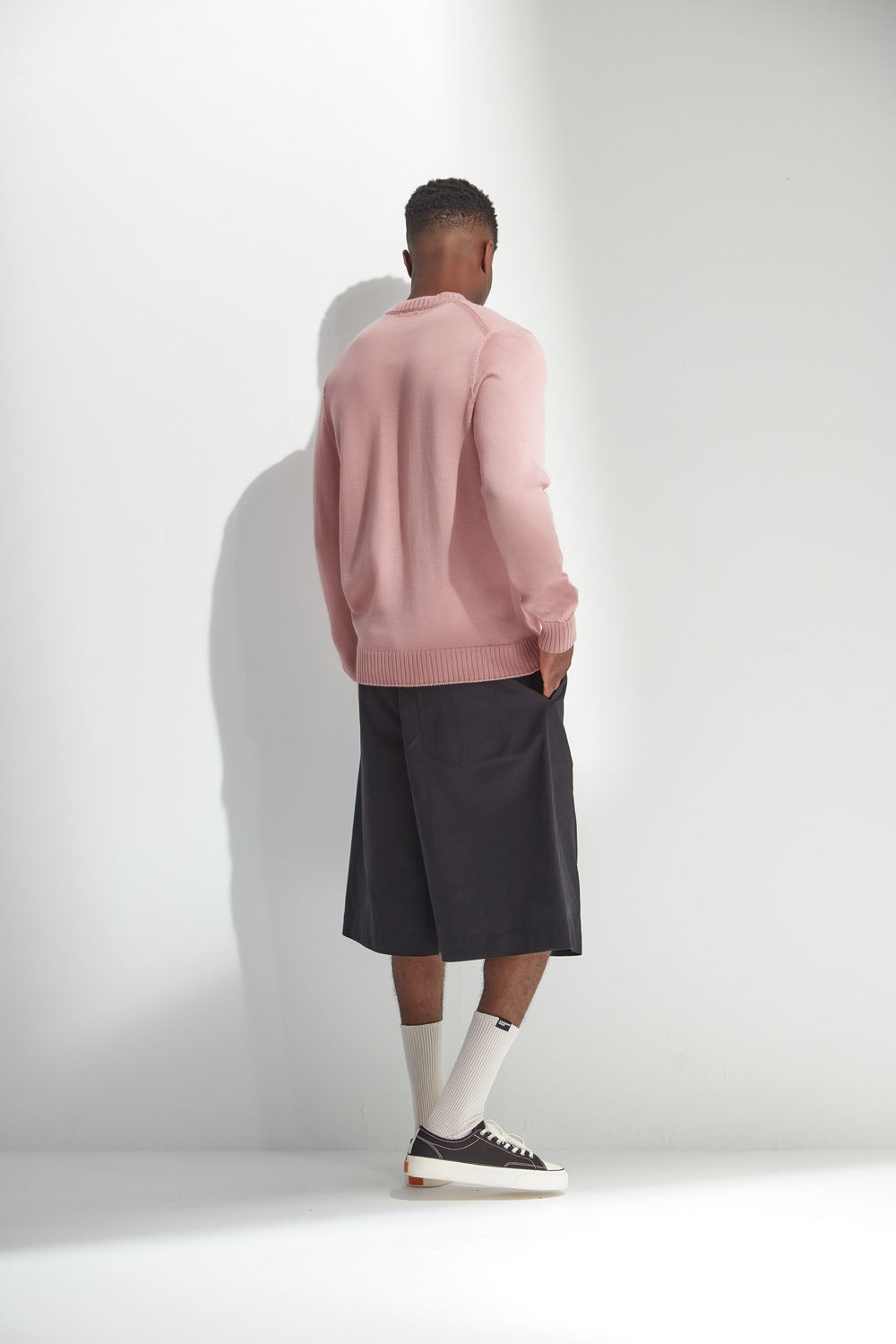 Man wearing a pink sweater and black shorts against a white background
