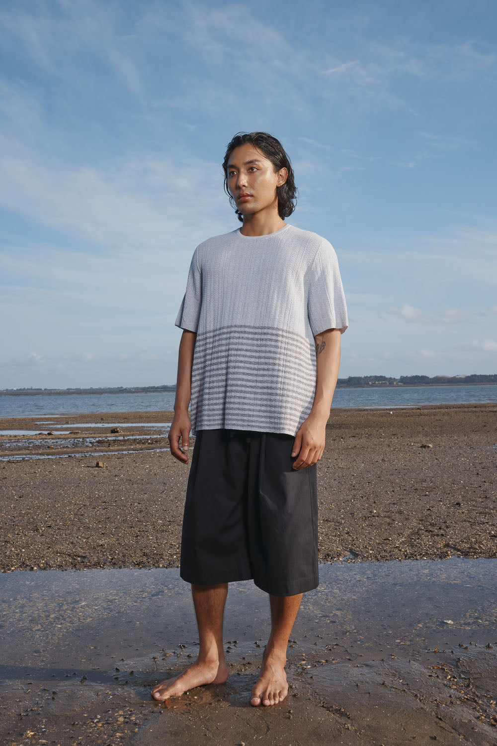 Man standing on a beach wearing a light gray t-shirt and black shorts.