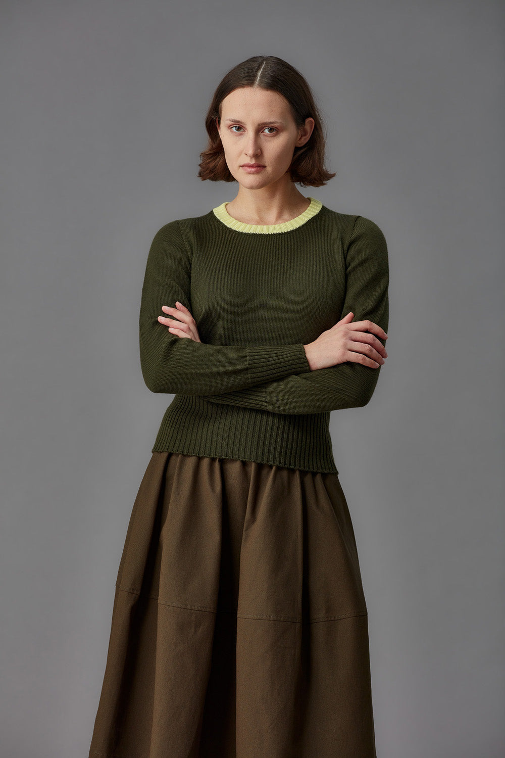 Woman wearing a green sweater with a yellow collar and brown skirt against a gray background