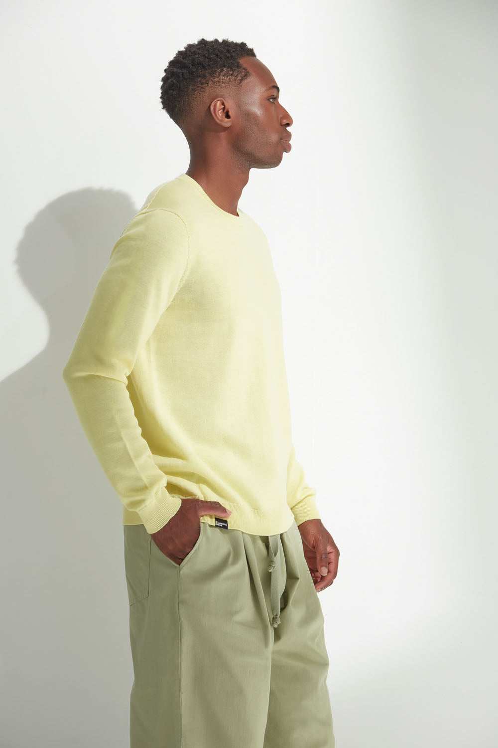 Man wearing a light yellow sweater and light green pants against a white background