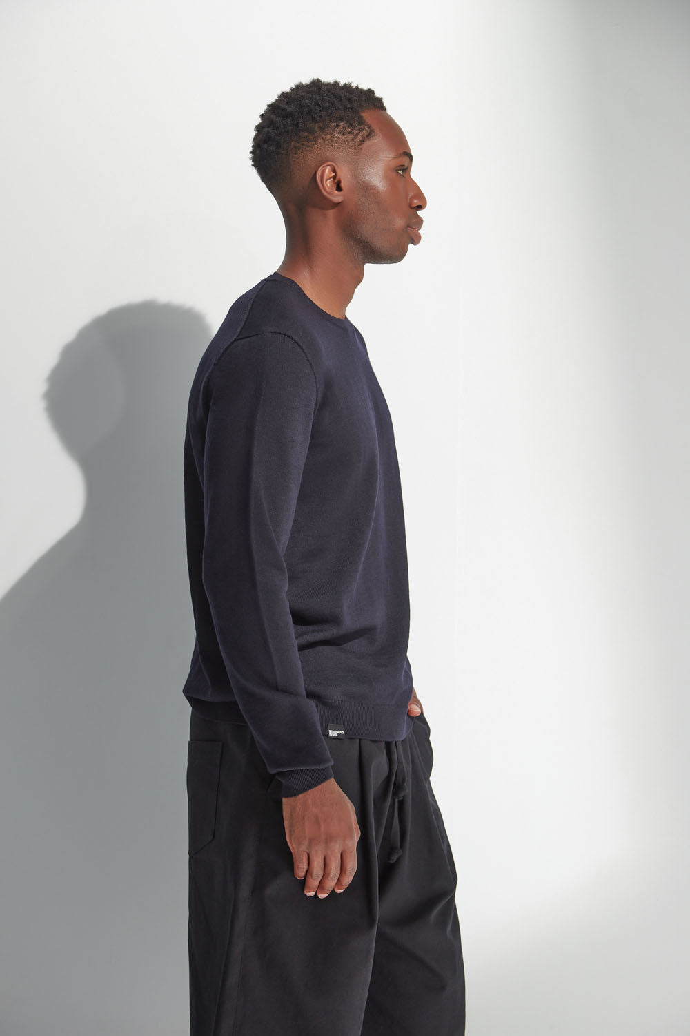 Man wearing a dark blue sweatshirt and black pants against a white background