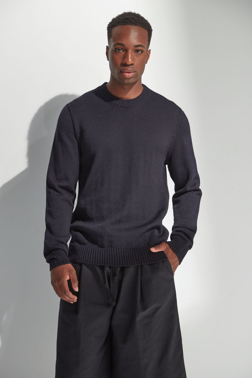Man wearing a dark navy sweater and pants against a white background