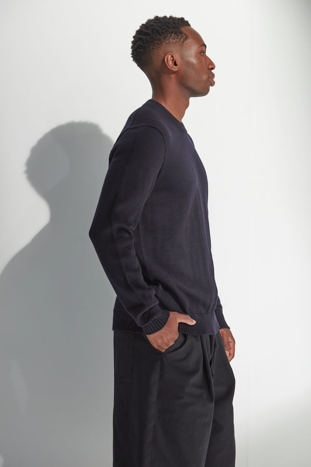 Man wearing a dark navy sweater and pants against a white background