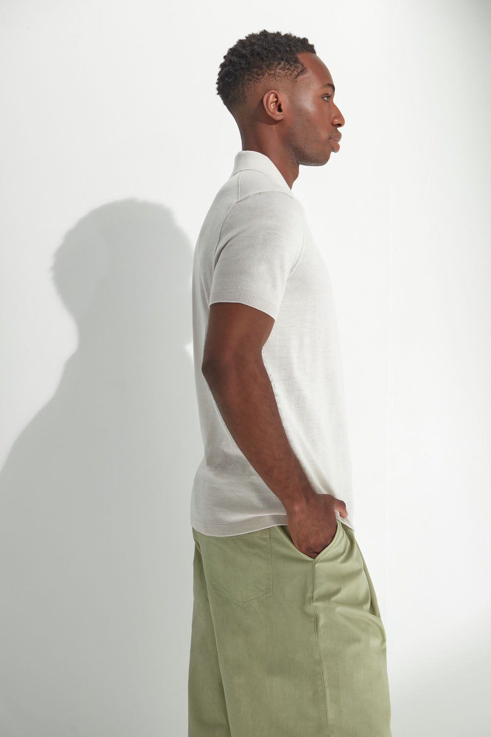 Man wearing a white polo shirt and light green pants against a plain background