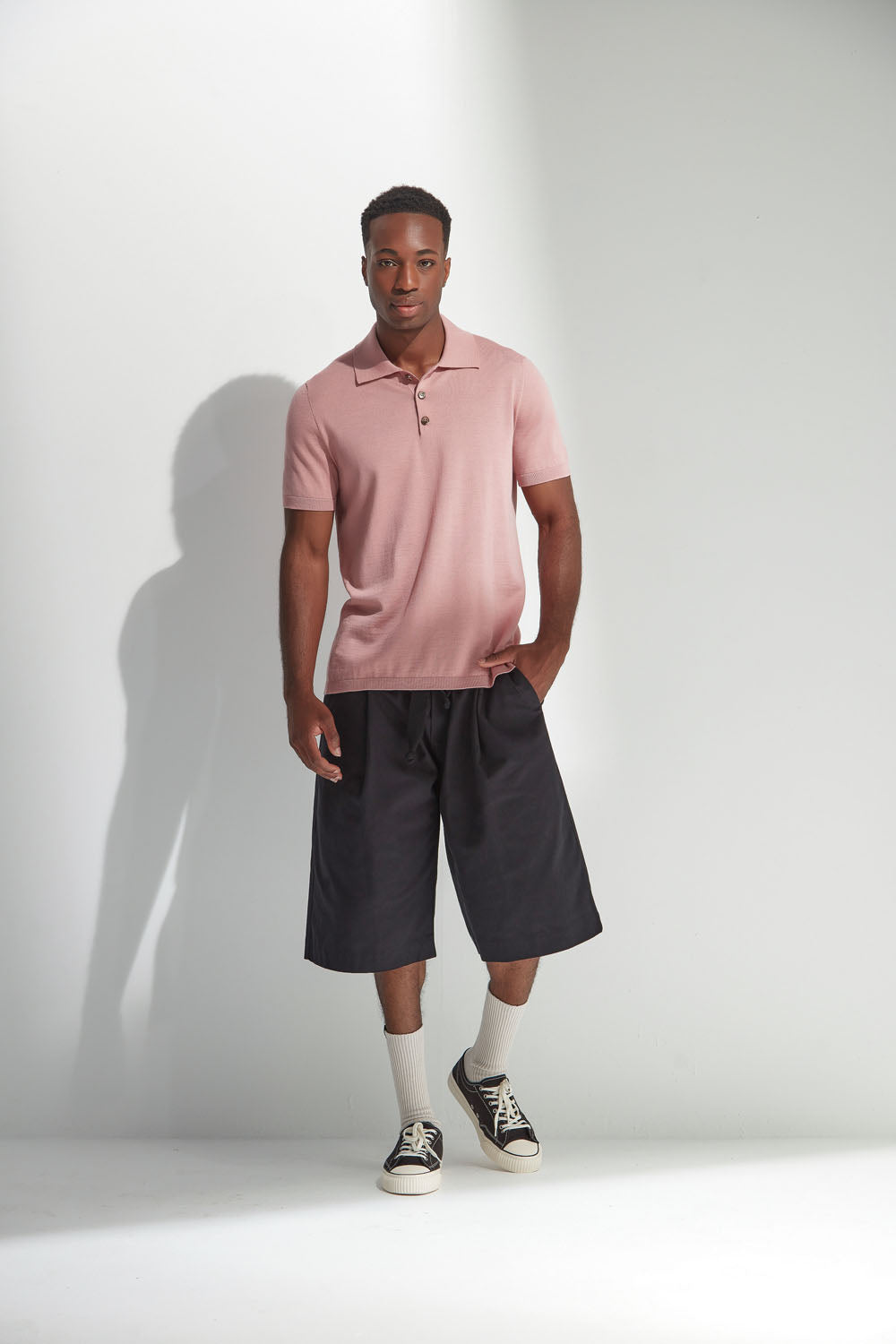 Man wearing a coral polo shirt and black shorts standing against a white background