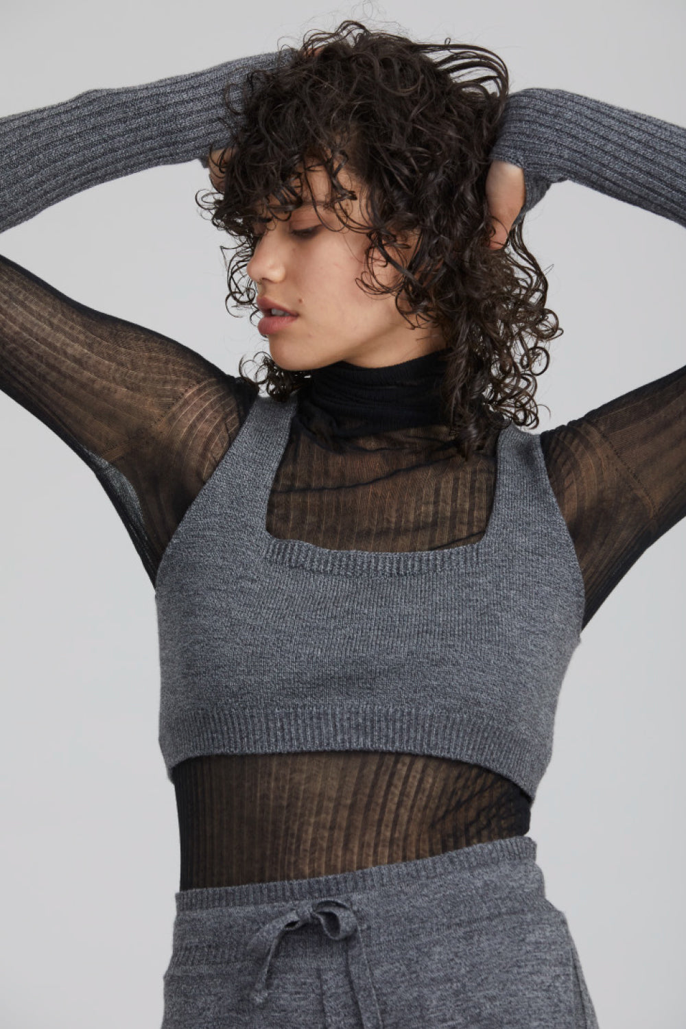 A woman standing wearing a marble-coloured Standard Issue Merino Little Crop Singlet.