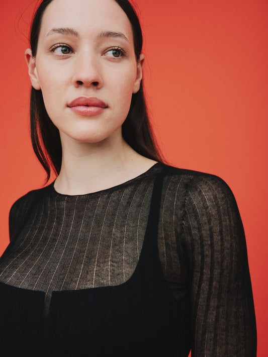 Woman wearing a black sheer tulle top against a red background