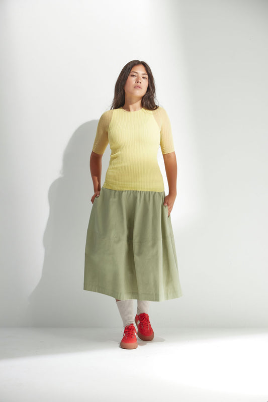 Woman wearing a yellow tulle top and green skirt on a white background
