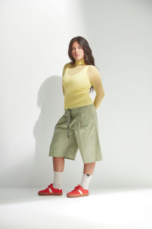 Person wearing a yellow tulle top and green shorts with red shoes on a white background