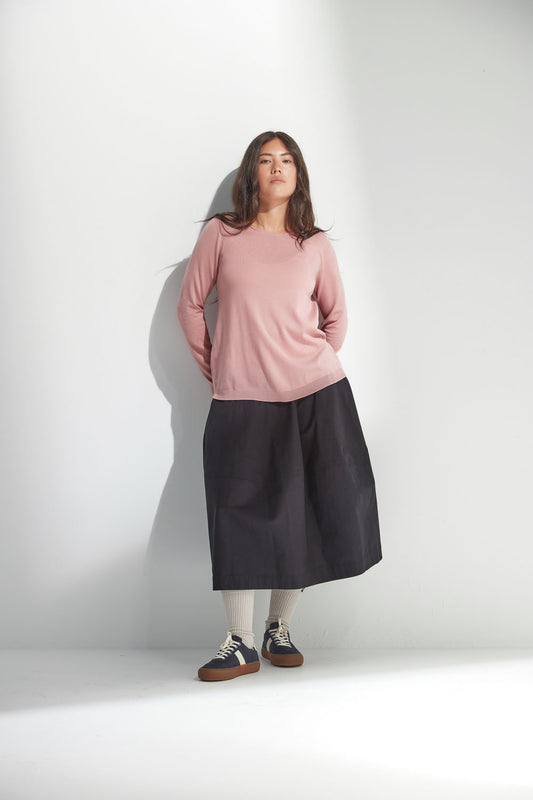 Woman wearing a pink top and black skirt against a white background
