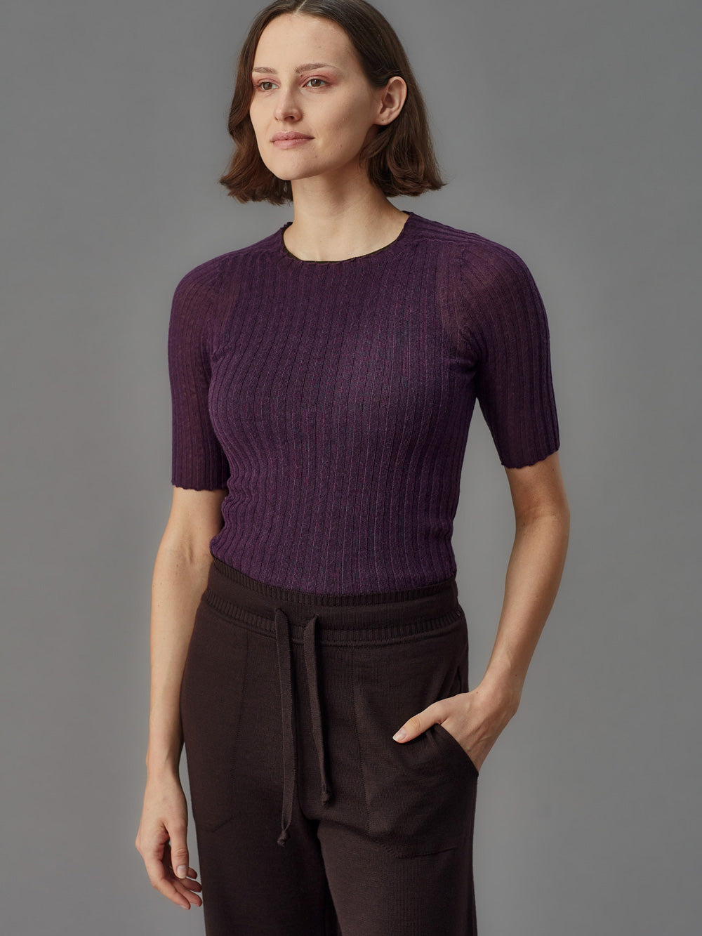 Woman wearing a purple tulle top and dark pants against a gray background