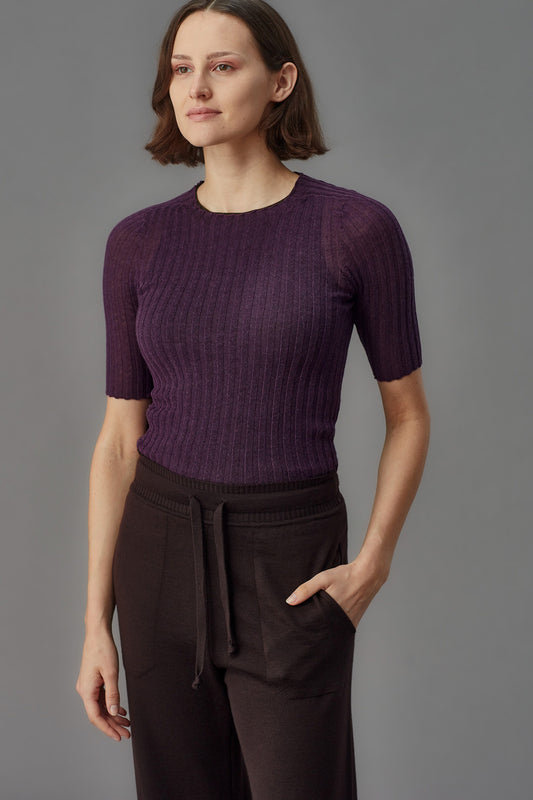 Woman wearing a purple merino ribbed tulle t-shirt and dark pants against a gray background