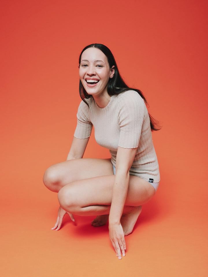 Woman wearing a pearl white merino tulle top against a orange background