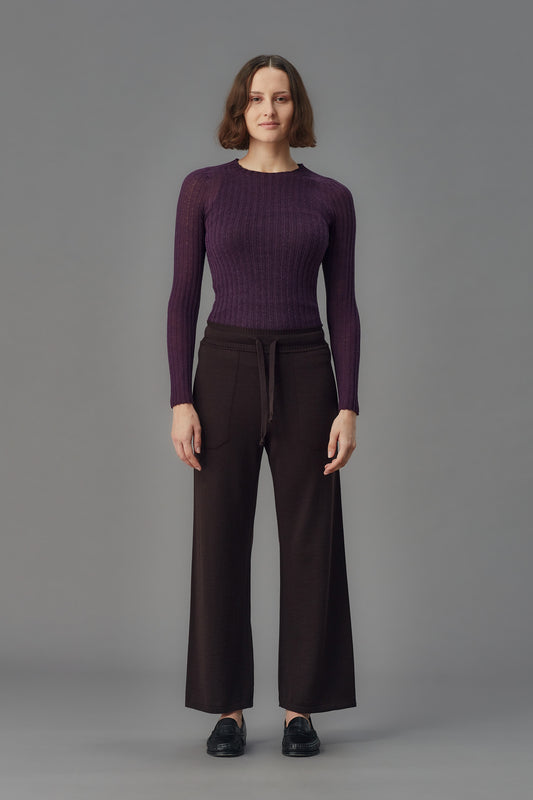 Person wearing a purple ribbed merino tulle and dark pants on a gray background