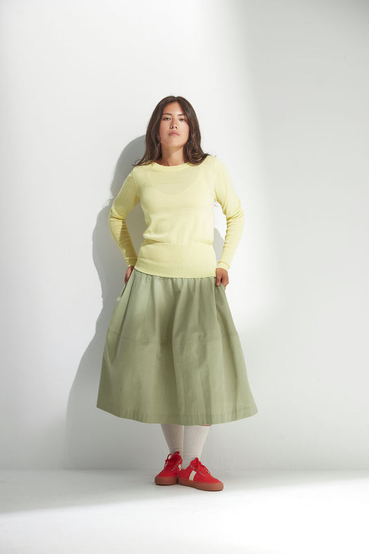 Woman wearing a light yellow sweater and green skirt against a white background