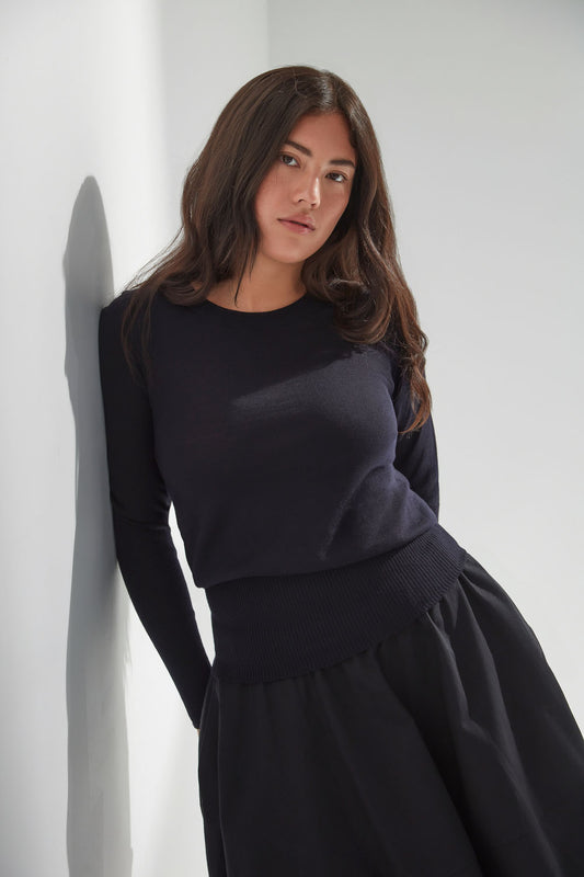 Woman wearing a navy sweater with a black skirt against a white background