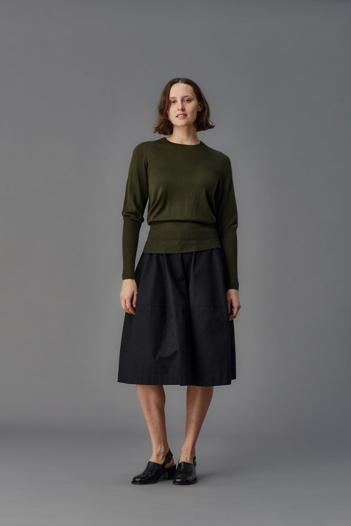 Woman wearing a green sweater and black skirt against a gray background