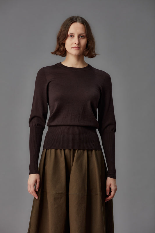 Woman wearing a brown sweater and skirt against a gray background