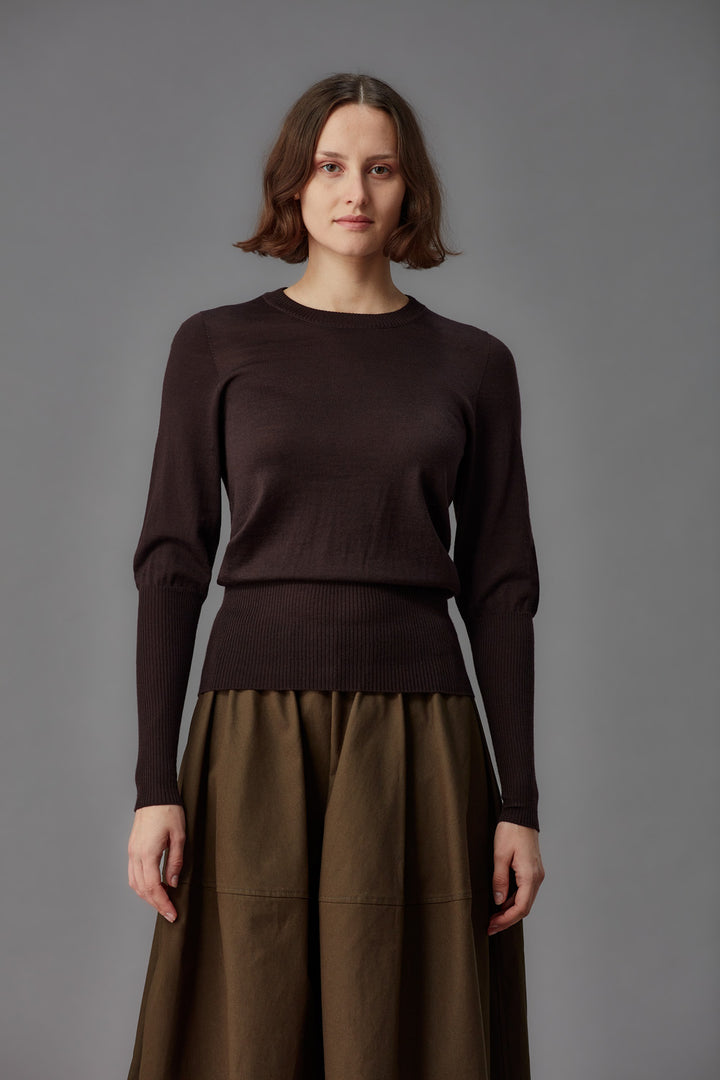 Woman wearing a brown sweater and skirt against a gray background