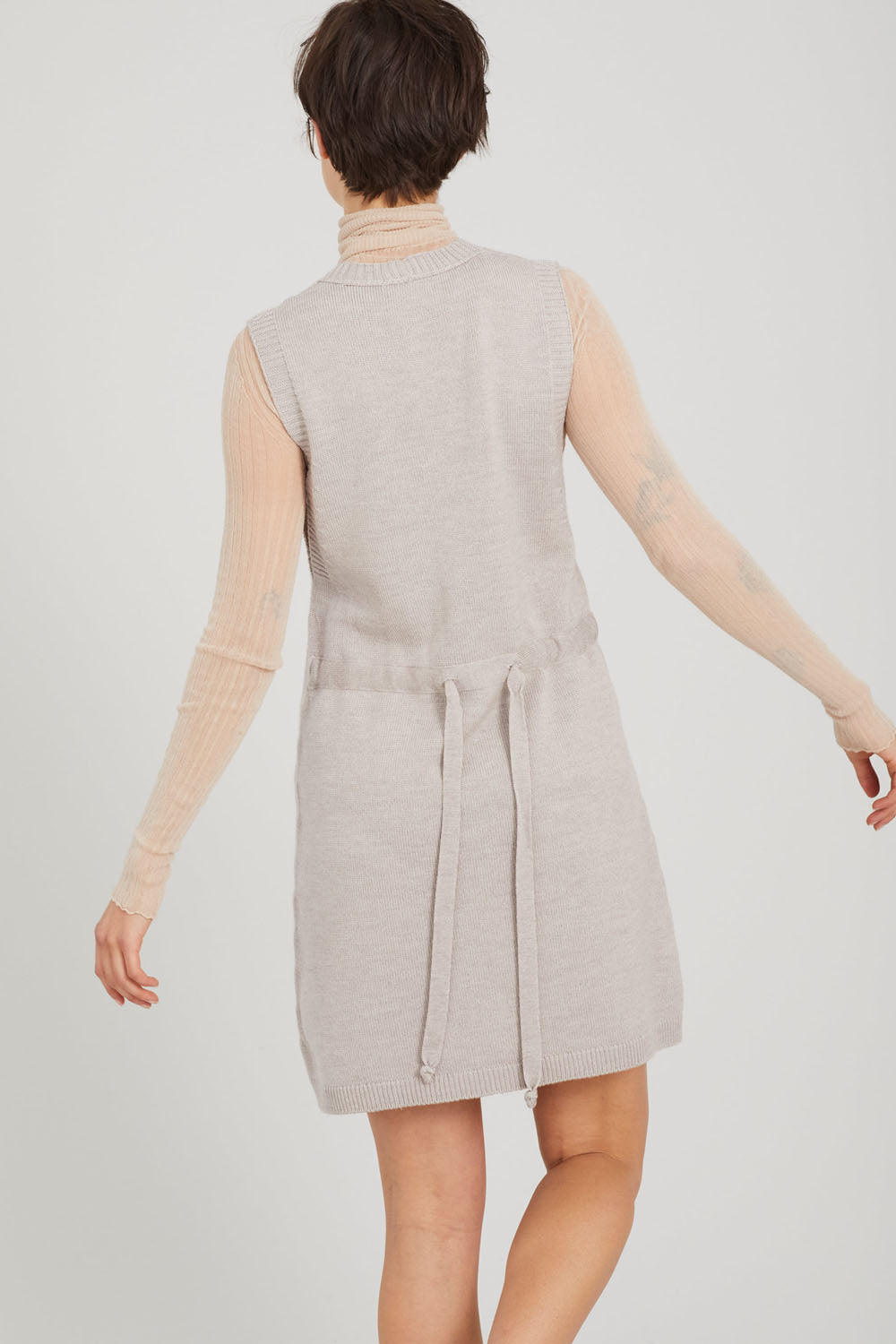 A woman facing away wearing a cashew-coloured Standard Issue Merino Pinafore dress.