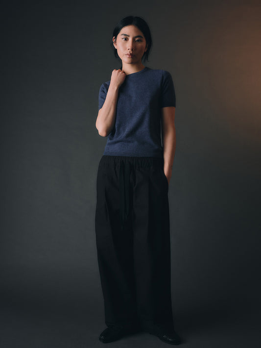 Woman wearing a blue cashmere top and dark pants against a dark background