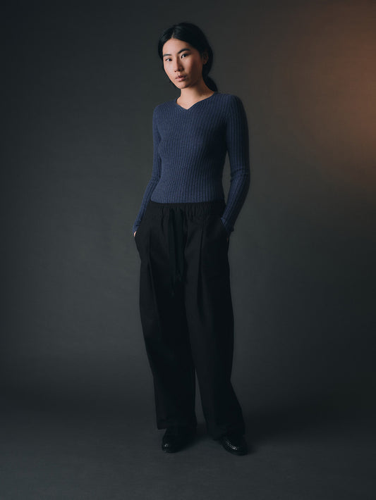 Woman wearing a blue cashmere sweater and dark pants against a gray background
