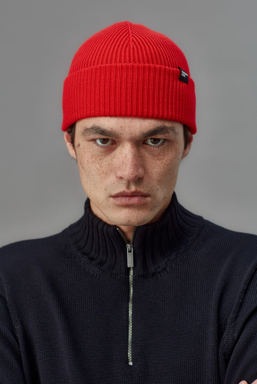 Man wearing a red beanie and dark sweater against a gray background